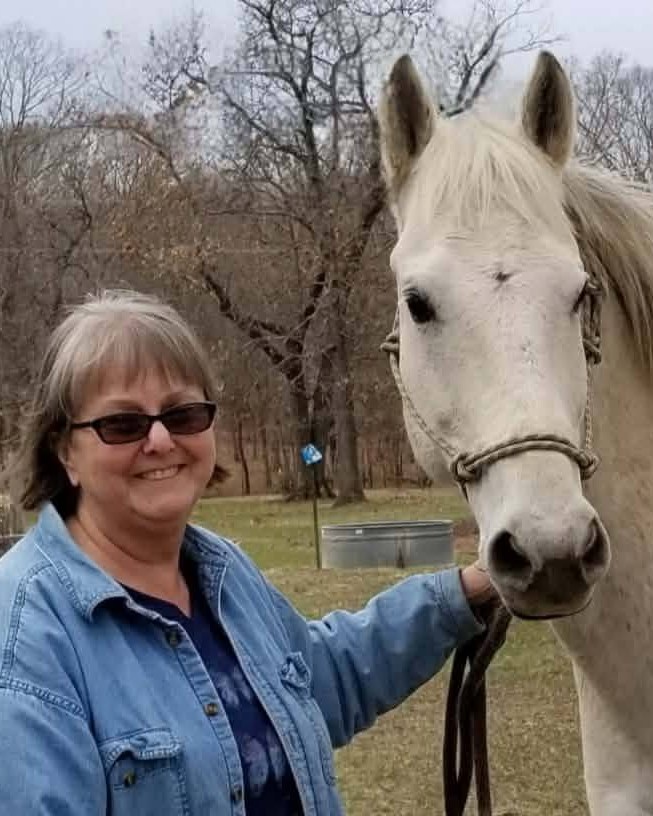 The founder's mom smiling beside a white horse